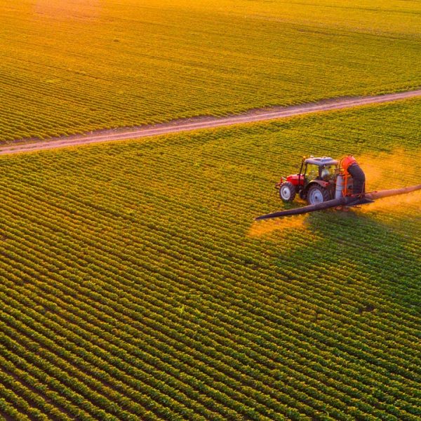 A tractor spraying a crop field in an orange glowing sunset