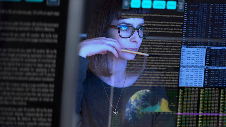 Close up of a woman wearing glasses and looking at lines of data on a screen