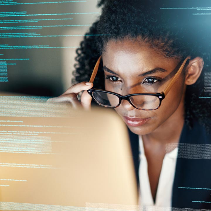 Close up of a woman wearing glasses and looking at lines of data on a screen