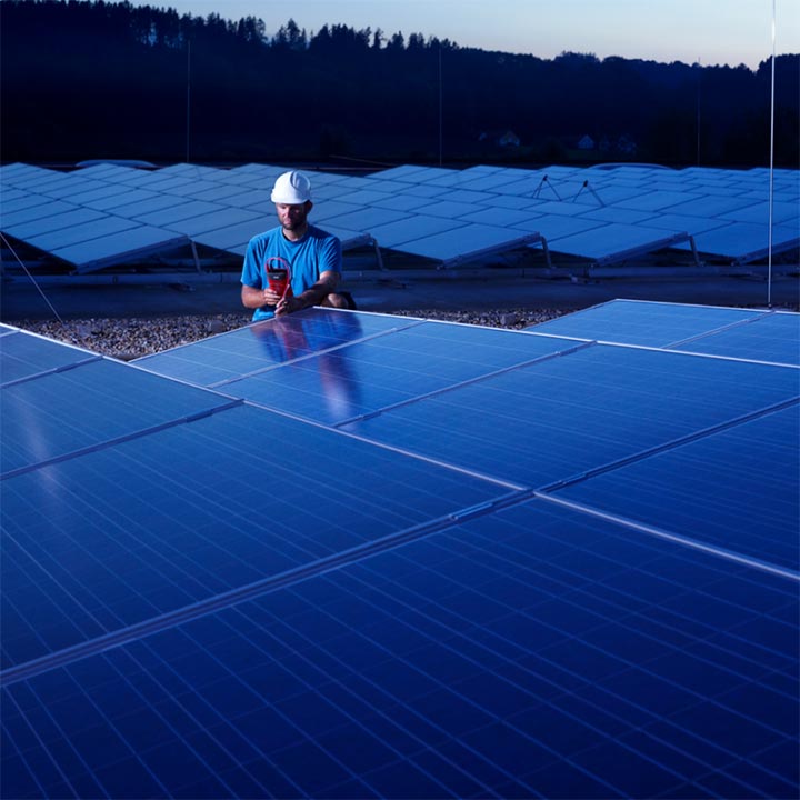 Man checking field of solar panels with digital testing equipment