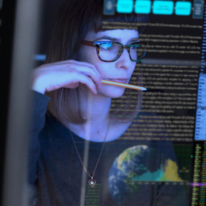 Another woman sitting at a computer terminal looking pensive holding a pencil in thought.