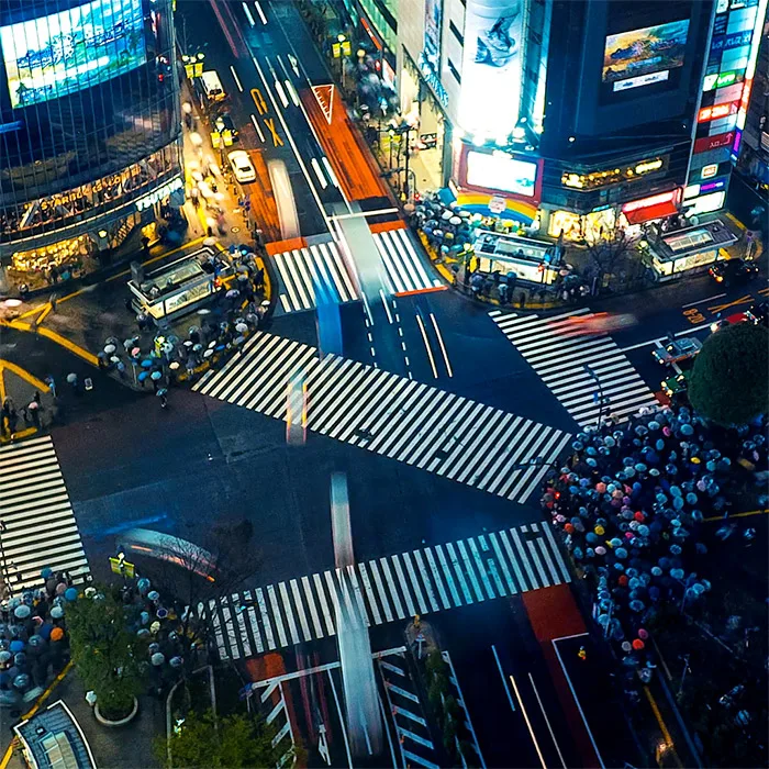 Shibuya crossing in Tokyo at night with crowds and cars and blurred lights showing dynamic movement